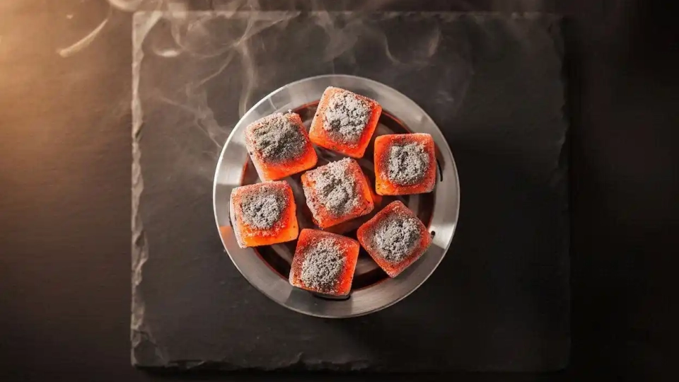 Glowing coconut shell hookah charcoal cubes on a heat management device showing steady heat performance for a smooth hookah session.